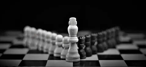 Een zwart-wit schaakbord met een koning die een formatie van pionnen aanvoert, als symbool voor leiderschap, strategie en tactische planning.